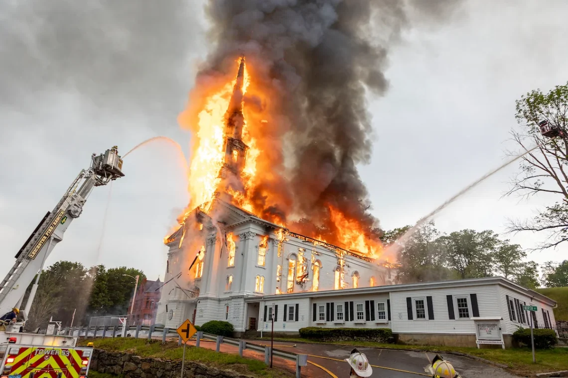 Church in flames with fire trucks spraying water from the left and right.